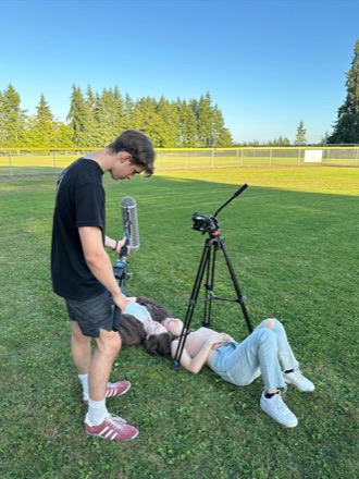 Filming a scene on a playing field, boom microphone over two actors lying in the grass